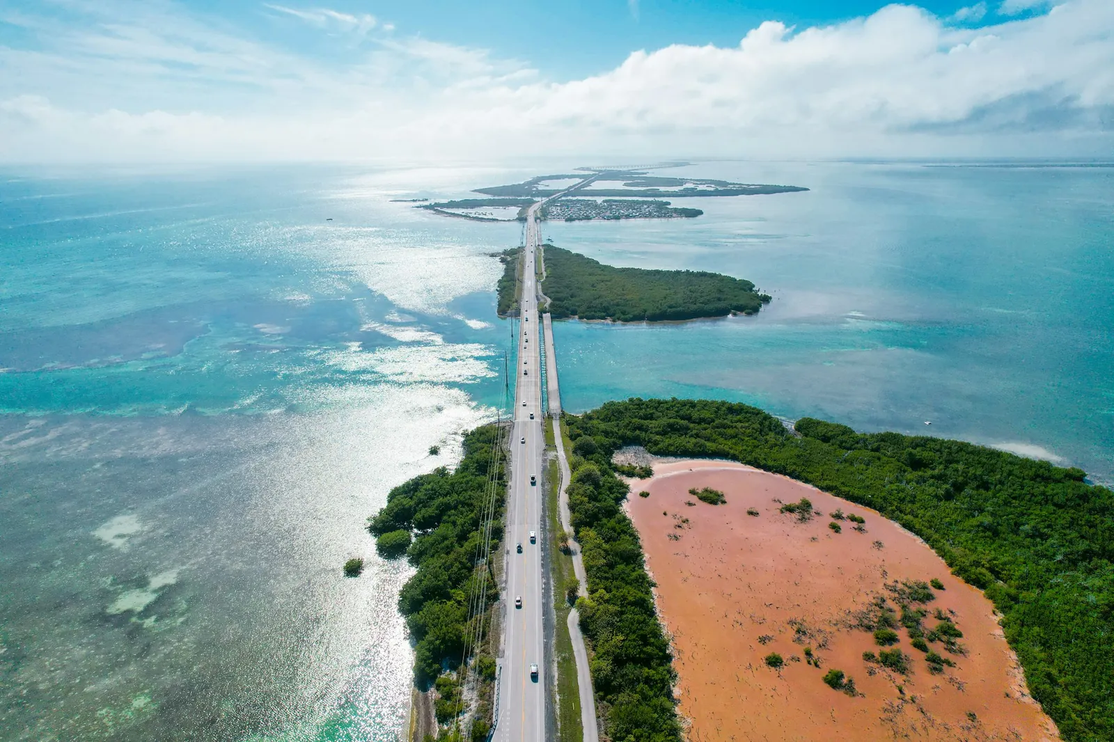 Drone view of the Overseas Highway (US-1, Florida Keys) running straight across turquoise water and mangrove islands, clouds on horizon