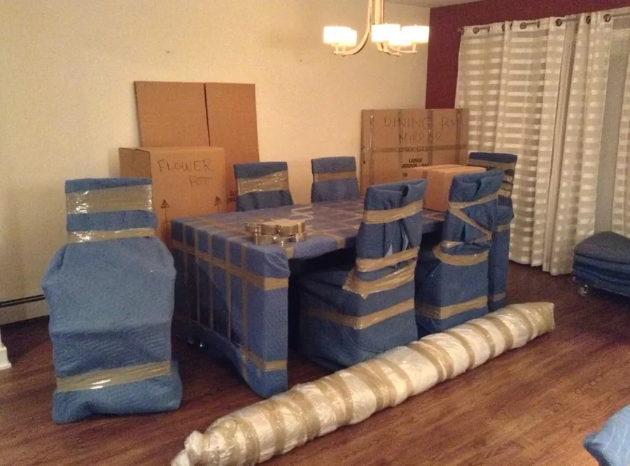 Dining table and chairs wrapped in blue moving blankets, ready to move